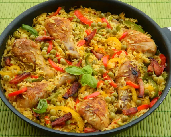 Pyszna paella z kurczakiem, ryżem, papryką i groszkiem w dużej patelni.