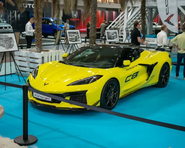 Jaskrawożółty Chevrolet Corvette C8 z czarnym dachem i felgami, prezentowany na niebieskiej podłodze wystawowej.