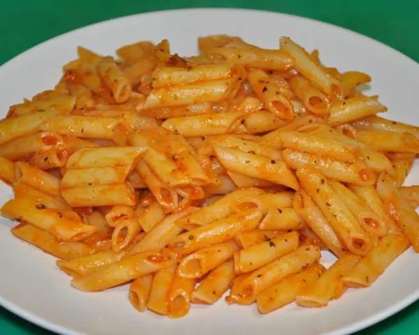 Macarrones penne con salsa de tomate y hierbas en un plato blanco.