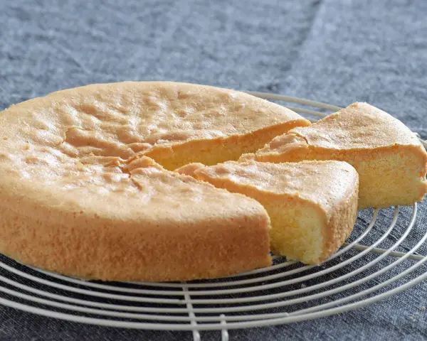 Bizcocho sin gluten esponjoso y dorado, recién cortado en porciones sobre una rejilla.