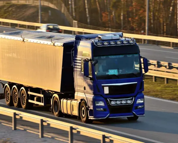 Niebieska ciężarówka z naczepą jedzie autostradą. Kierowca posiada świadectwo kwalifikacji zawodowej, co pozwala mu na bezpieczne przewożenie towarów.