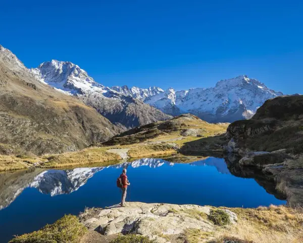 Randonneur contemplant un lac alpin aux reflets parfaits, un paysage grandiose qui pourrait faire partie d'un GR5 itinéraire complet.
