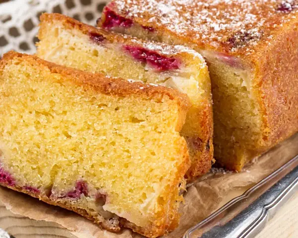 Puszyste ciasto z serka wiejskiego z malinami, posypane cukrem pudrem. Idealne na podwieczorek.