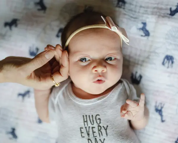 Uroczy 3 tygodniowy noworodek w body z napisem "HUG EVERY DAY", z delikatną opaską na głowie.