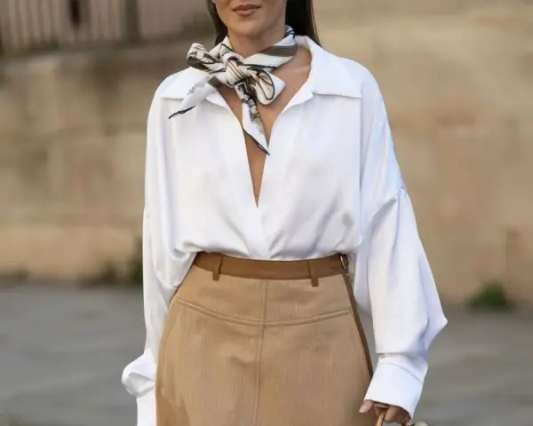 Elegancka biała koszula i beżowa spódnica to świetne **stylizacje jak ukryć brzuch**. Wzorzysty szalik dodaje szyku.