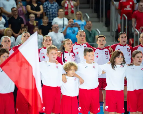 Młode zawodniczki i zawodnicy w strojach reprezentacji Polski, z biało-czerwoną flagą, przed meczem piłka ręczna kobiet mistrzostwa świata.