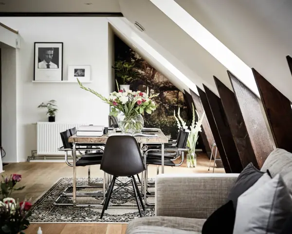 Välkomnande inredd vindsvåning med snedtak, matplats med blommor och konst.