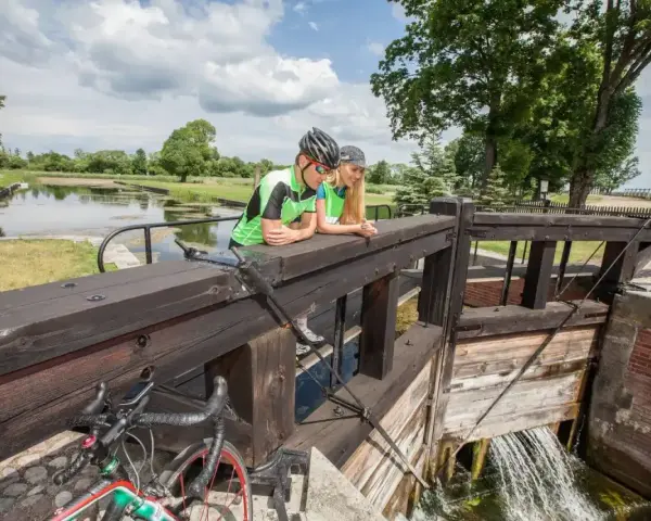 Para rowerzystów odpoczywa przy śluzie, podziwiając malownicze **trasy rowerowe Augustów**.