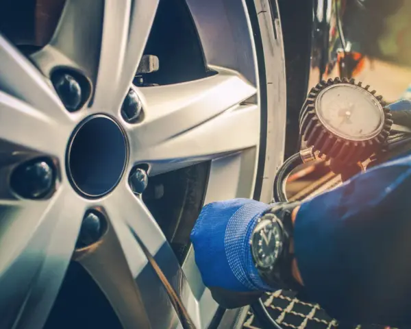 Controllo pneumatici con manometro su cerchio Ford. Guanto blu e orologio da polso.