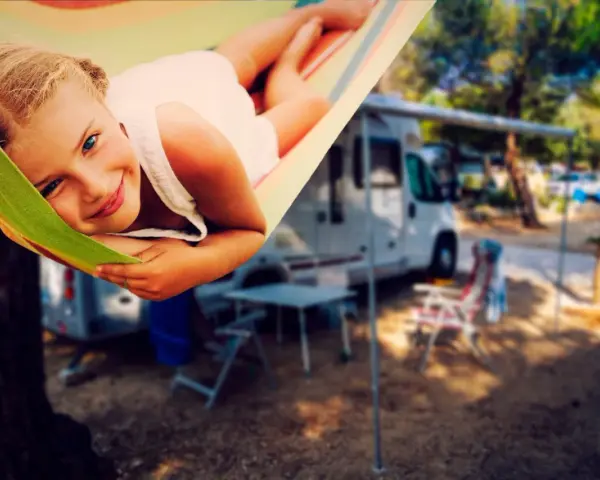 Ein glückliches Mädchen entspannt sich in einer Hängematte auf einem familienfreundlichen Campingplatz. Im Hintergrund stehen Wohnmobile und Campingmöbel.