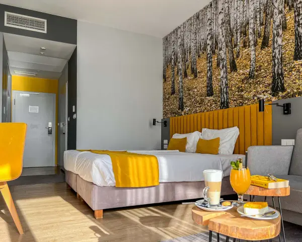 Pokój hotelowy z motywem lasu, żółtym akcentem i napojami. Idealne miejsce na relaks, jak sugerują notera hotel spa opinie.