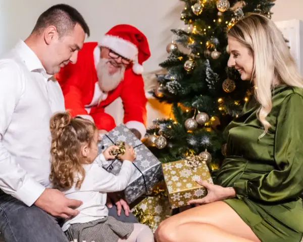 Rodzina otwiera prezenty przy choince, a Mikołaj uśmiecha się w tle. Wesołe święta w hotelu.