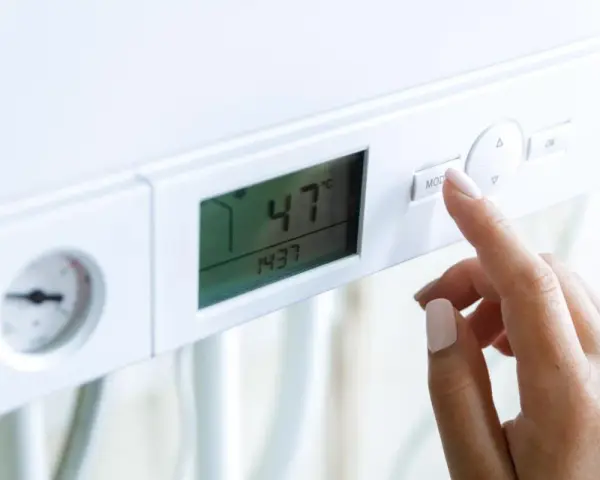 Dito, la mano preme il pulsante "MOD" su una caldaia. Il display mostra 47°C, ma la pressione acqua calda è bassa.
