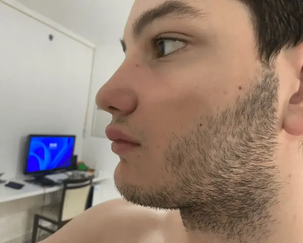 Perfil de un joven con barba incipiente, preparándose para afeitar barba. Al fondo, un monitor con pantalla azul.
