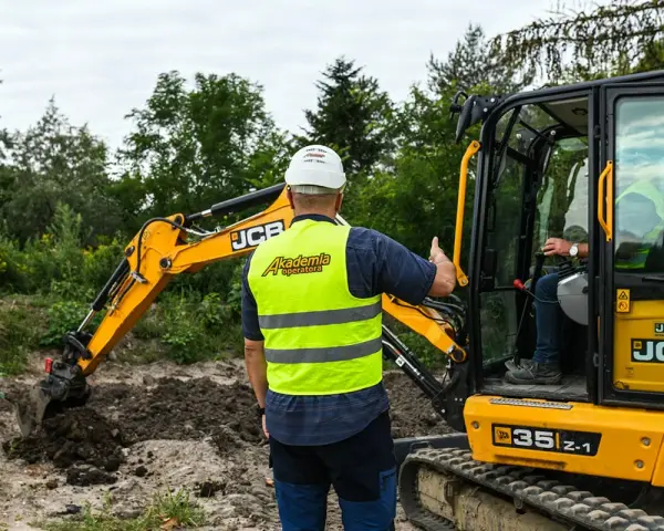 Szkolenie na koparkę w Akademii Operatora. Instruktor w kamizelce odblaskowej pokazuje, jak uzyskać uprawnienia na koparkę.