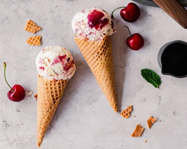 Zwei Waffelhörnchen mit Joghurt Kirsch Eis, garniert mit frischen Kirschen und Minze.
