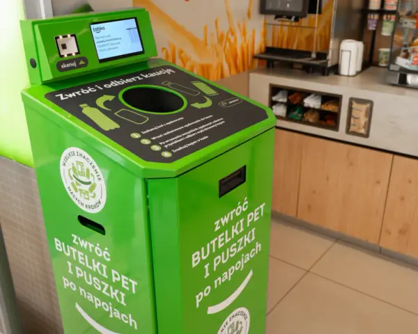 Zielony automat do zwrotu butelek PET i puszek. Skanuj kod, wrzuć opakowanie, by zdjąć zabezpieczenie sklepowe z butelki i otrzymać kaucy.