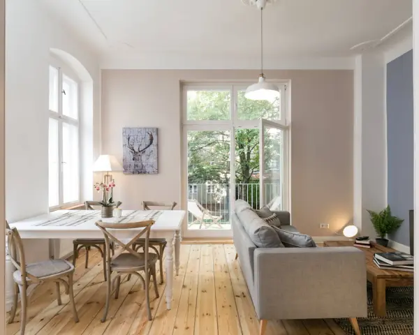 Gemütliches 15 qm Wohnzimmer mit Essbereich einrichten: heller Esstisch, graue Stühle, Sofa, Holzboden, Fenster mit Blick ins Grüne.