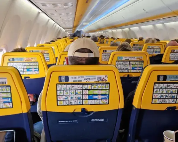 Widok wnętrza samolotu Ryanair z żółtymi oparciami siedzeń i instrukcjami bezpieczeństwa.