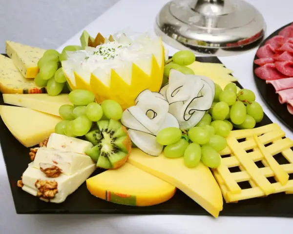 Plateau de fromage festif avec raisins verts, kiwi, noix et charcuterie. Une belle décoration plateau de fromage pour un événement.