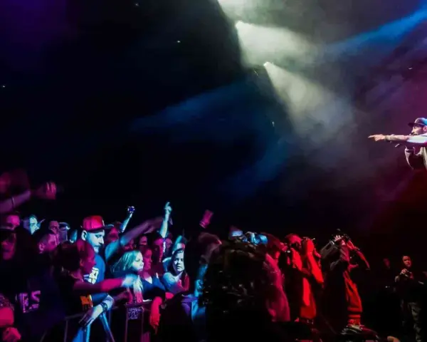Raper na scenie, w świetle reflektorów, wskazuje palcem na tłum. Koncert w **3 wymiar**ze, pełen energii i emocji.