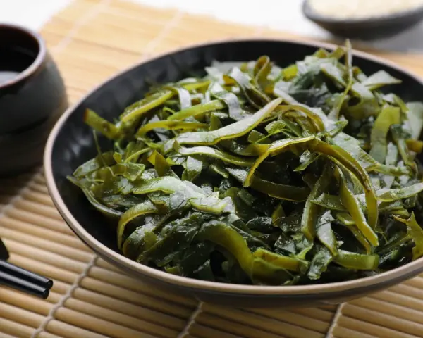 Un bol de salade d'algues kombu, aux multiples algue kombu bienfaits, servi avec une sauce et des baguettes sur un tapis de bambou.