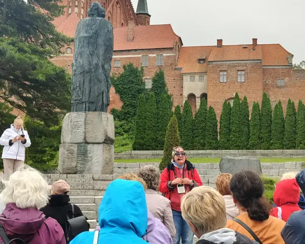 Grupa turystów słucha przewodnika przy pomniku Kopernika. To jedna z wielu atrakcji Warmii, gdzie historia ożywa.