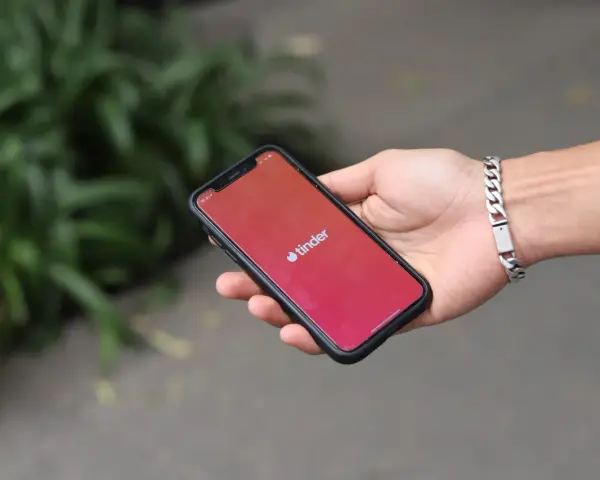 Dłoń trzyma smartfon z logo Tinder. Zastanawiasz się, czy Tinder jest płatny? Aplikacja oferuje darmowe funkcje, ale płatne subskrypcje dają więcej możliwości.