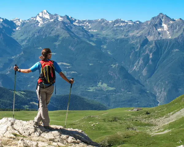 Donna con zaino e bastoncini da trekking ammira i maestosi **sentieri Valle d'Aosta** e le cime innevate.