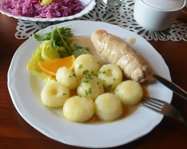 Pyszne kluski śląskie z roladą mięsną, surówką z czerwonej kapusty i plasterkiem pomarańczy.