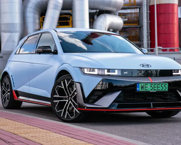Jasnoniebieski Hyundai IONIQ 5 N z czarnymi akcentami i czerwonymi detalami, zaparkowany przed przemysłową instalacją.