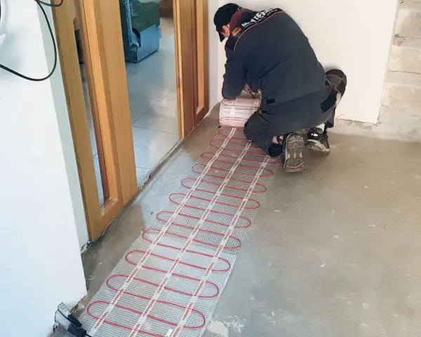 Instalator montuje matę grzewczą, przygotowując ogrzewanie elektryczne podłogi.