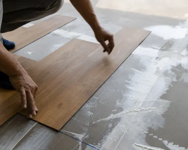 Hände legen Holzoptik-Vinylboden auf Kleber. Das Verlegen von Vinylboden erfordert Präzision.
