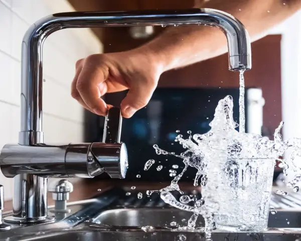 Mano girando la llave para cuidar el agua, que salpica al llenar un vaso.
