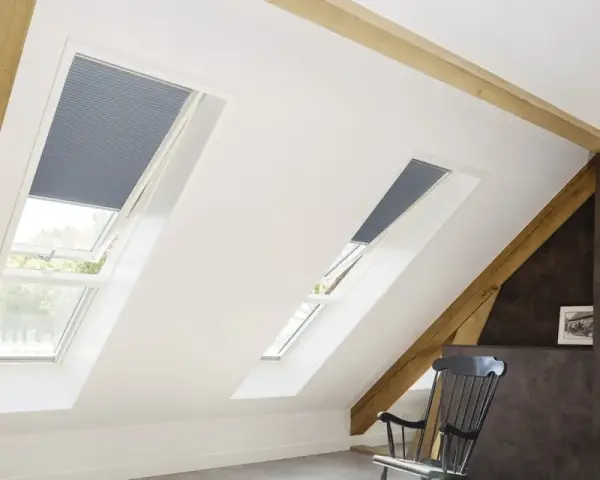 Schicke Dachfenster mit Plissees verkleiden. Holzbalken und ein gemütlicher Schaukelstuhl schaffen eine warme Atmosphäre.