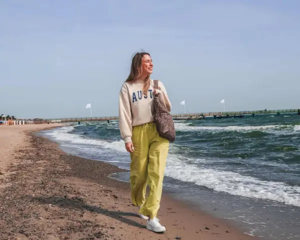 Frau spaziert am stein strand entlang, die Wellen rauschen.