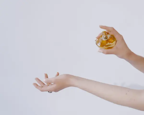 Dłoń trzymająca perfumy nad drugą dłonią.