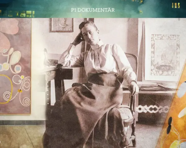 En kvinna sitter vid ett skrivbord, omgiven av färgstarka hilma af klint-konstverk.