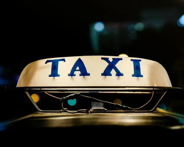 Tetto di un taxi con la scritta "TAXI" in blu. La luce soffusa e i riflessi suggeriscono la notte, un momento in cui ci si interroga quanto guadagnano i tassisti.