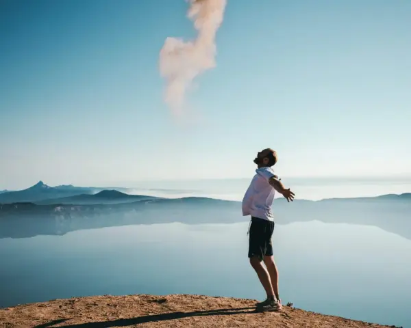 Mann mit ausgebreiteten Armen auf einem Felsvorsprung, der Rauch in den Himmel stößt. Ein Moment der Freiheit, wie Gottes Gunst.