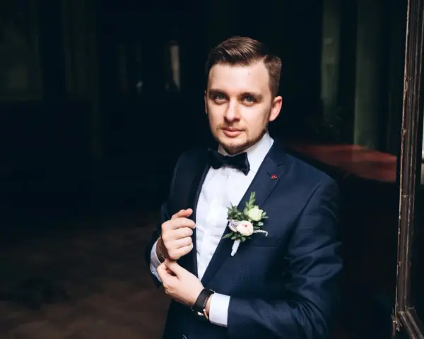 Elegancki mężczyzna w granatowym smokingu z kamizelką, z butonierką.