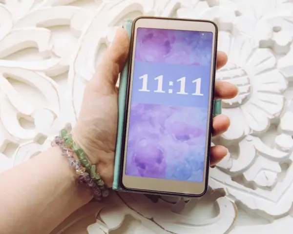 Dłoń trzyma telefon z wyświetloną godziną 11:11, co może mieć szczególne znaczenie.