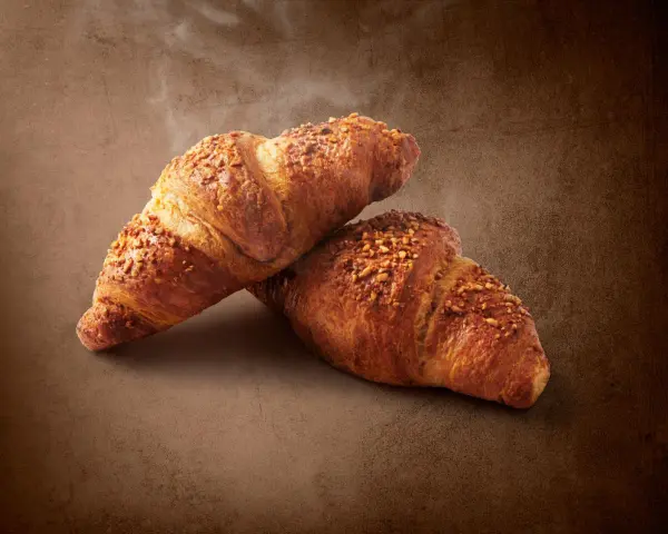 Dwa chrupiące croissanty posypane orzechami. Pyszna przekąska, ale warto pamiętać o ich kaloryczności - croissant kcal.