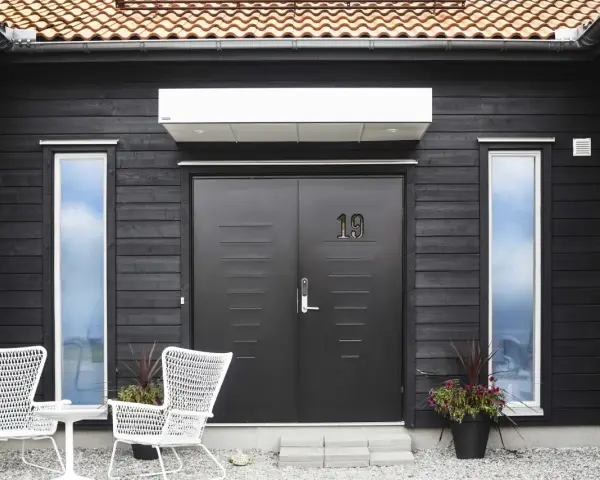 Svart trähus med dubbeldörr, nummer 19, och vita stolar. En fin inspiration framsida hus med moderna detaljer.