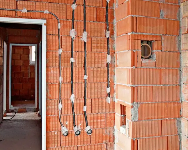 Instalacja elektryczna w trakcie budowy: łączenie kabli w ścianie bez puszki, widoczne przewody i otwory w cegłach.