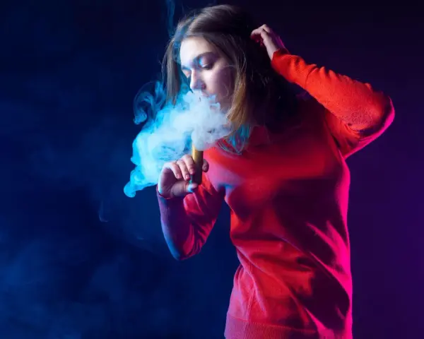 Joven exhala humo azul de un vaper. El vaper con nicotina es malo para la salud.
