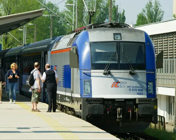 Pasażerowie czekają na pociąg PKP Intercity, gotowi do podróży z biletem wakacyjnym.