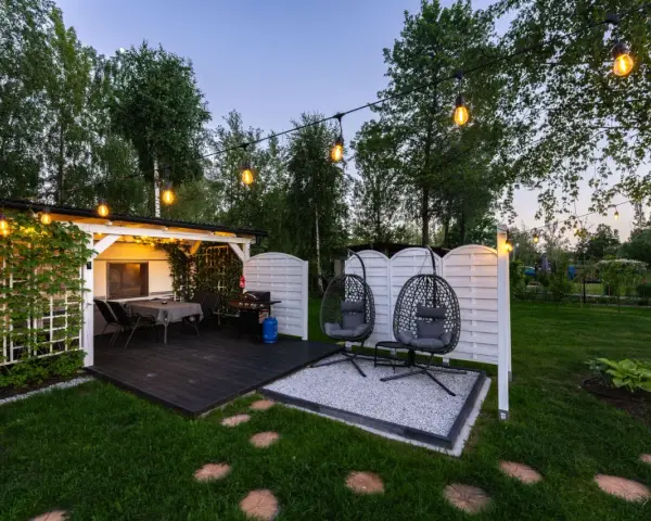 Idealne miejsce na camping w Ochabach: zadaszony taras z grillem, stolikiem i wiszącymi fotelami. Wieczorem rozświetla go girlanda żarówek.