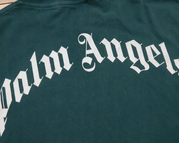Zielona koszulka Palm Angels z białym, stylizowanym napisem.