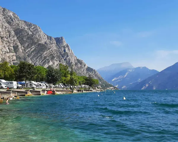 Malowniczy camping nad jeziorem Garda, z kamperami przy brzegu i górami w tle.
